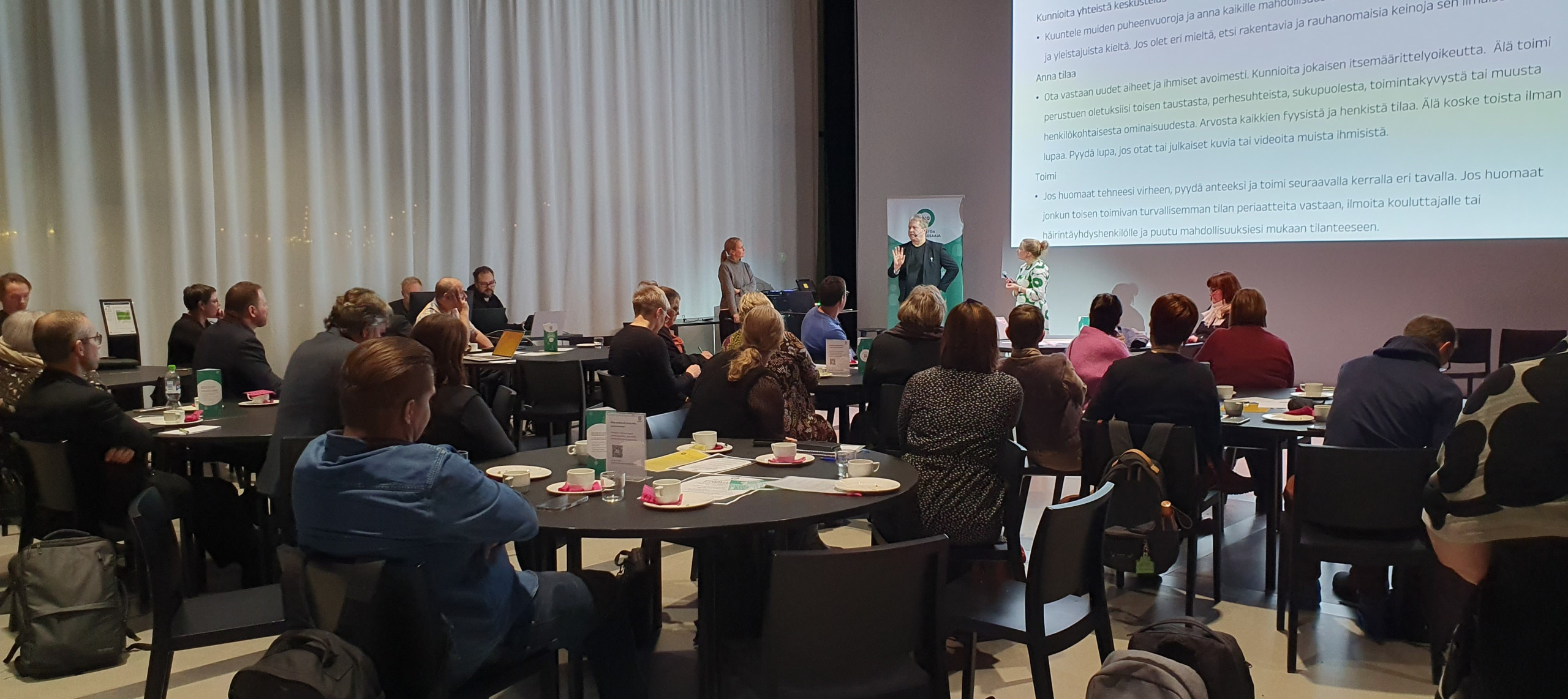 Ihmisiä seminaaritilassa kuuntelemassa puhujaa.