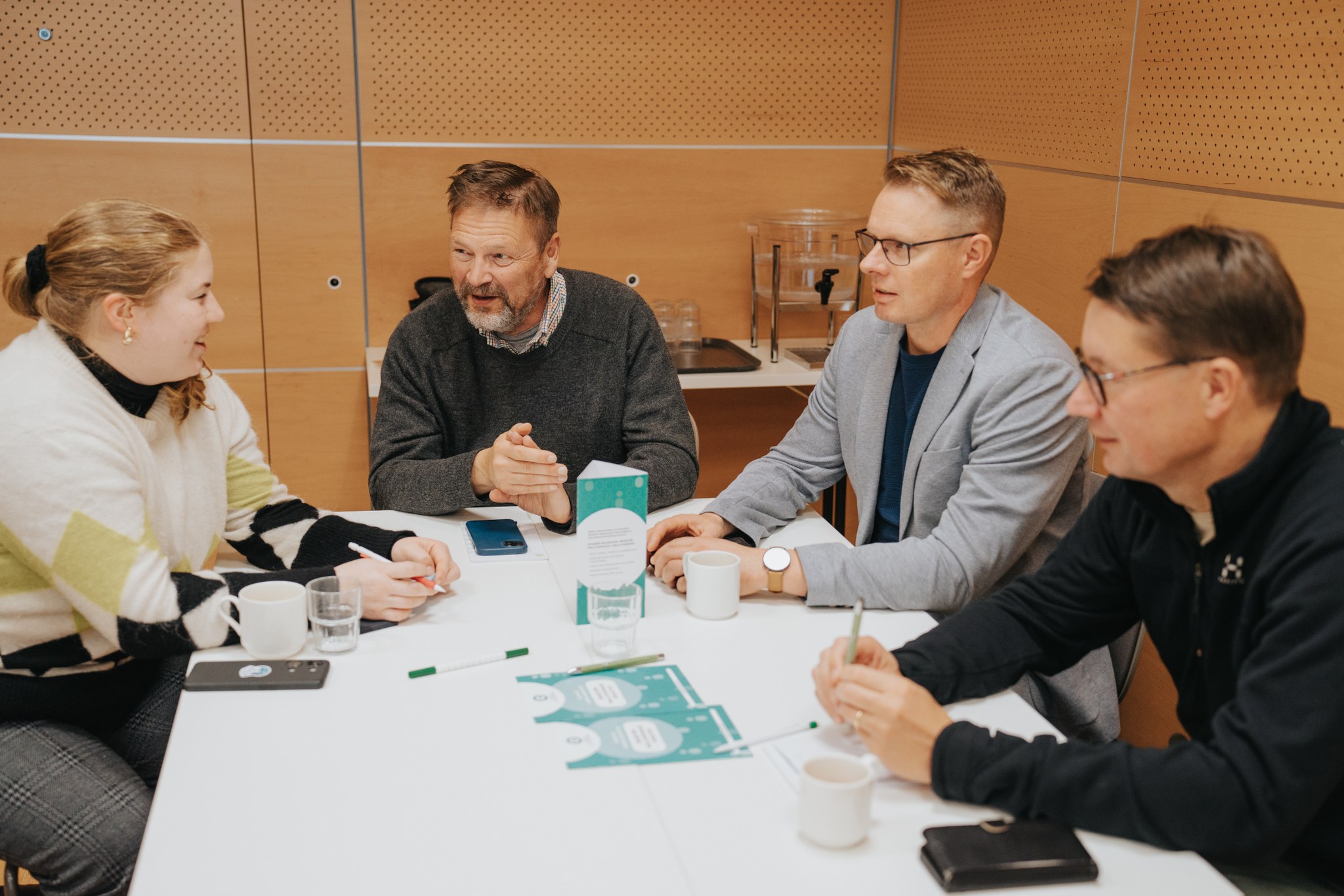 Neljä henkilöä keskustelee pöydän ympärillä.
